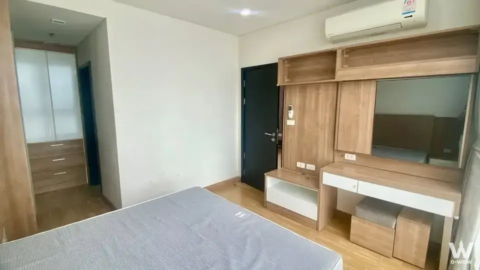 The bedroom has a bare mattress, light oak wardrobe and black door in a 1-bed Le Luk Condominium