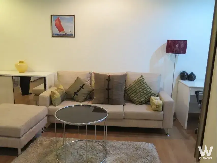 Bright living room in The Address Sukhumvit 42 with beige sectional sofa, chrome accents, and shaggy rug