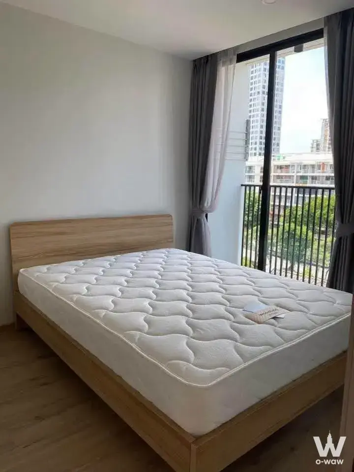 Bright bedroom in Serio Sukhumvit 50 featuring a light-oak platform bed and balcony access