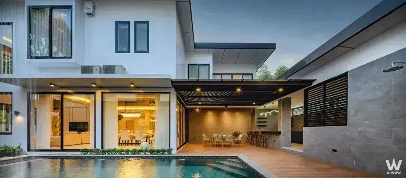 Two-story villa exterior in The Urban Oasis Bangkok showing a pool deck, pergola, and glass doors at twilight