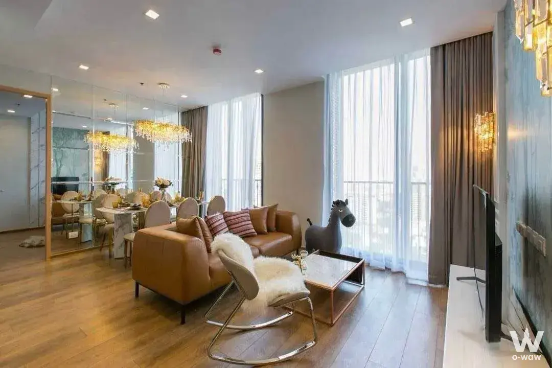 Spacious living and dining area in Noble BE33 with a leather sofa, crystal chandelier, and blue-grey accent wall