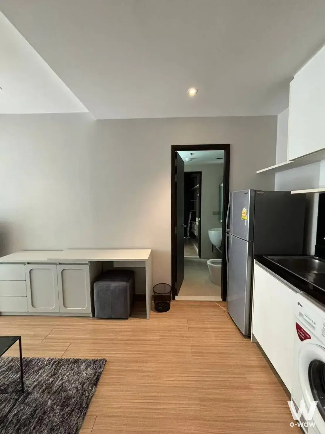 Sky Walk Residences studio unit with light wood flooring, white media console, and integrated kitchenette
