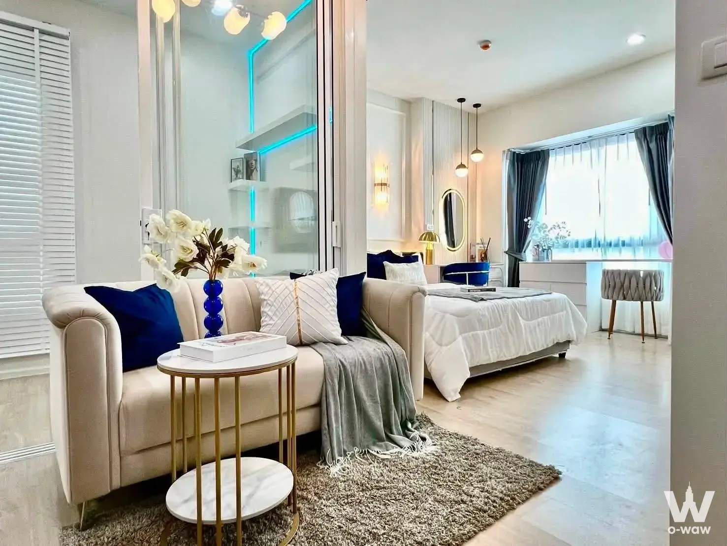 Open-plan studio in S1 Rama 9 Condominium featuring cream seating, navy accents, and gold-framed decor