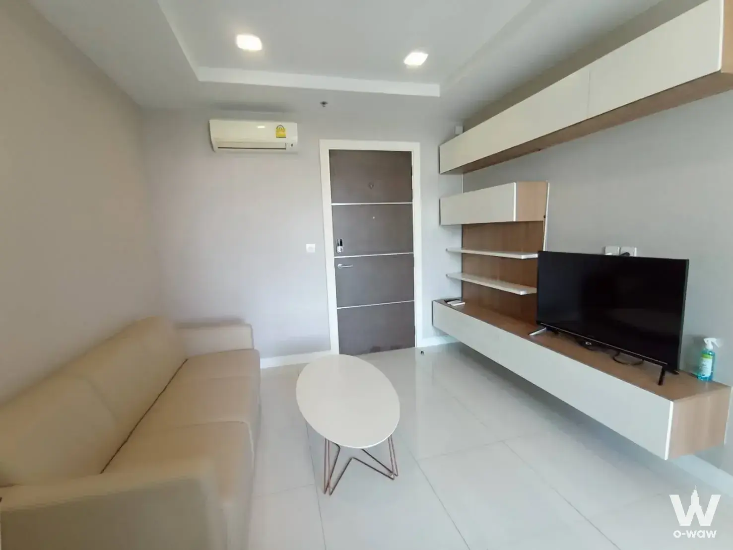 Spacious living room in The Metropolis Samrong sale listing with beige leather sofa and built-in media wall