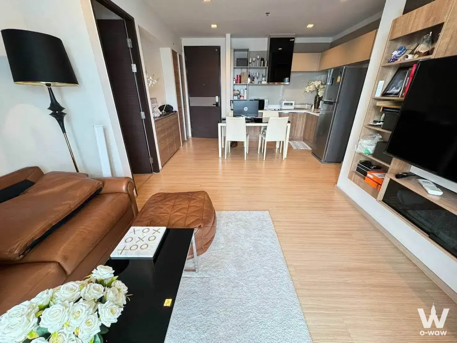 Open-plan living room with tan leather sofa and dining set in a furnished RHYM Sathorn condo