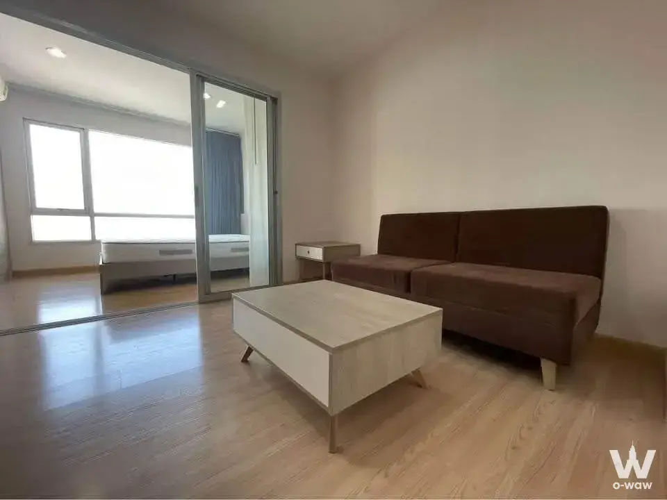 Open plan living room in A Plus 2 Rattanathibet condo featuring dark sofa and mirrored sliding doors