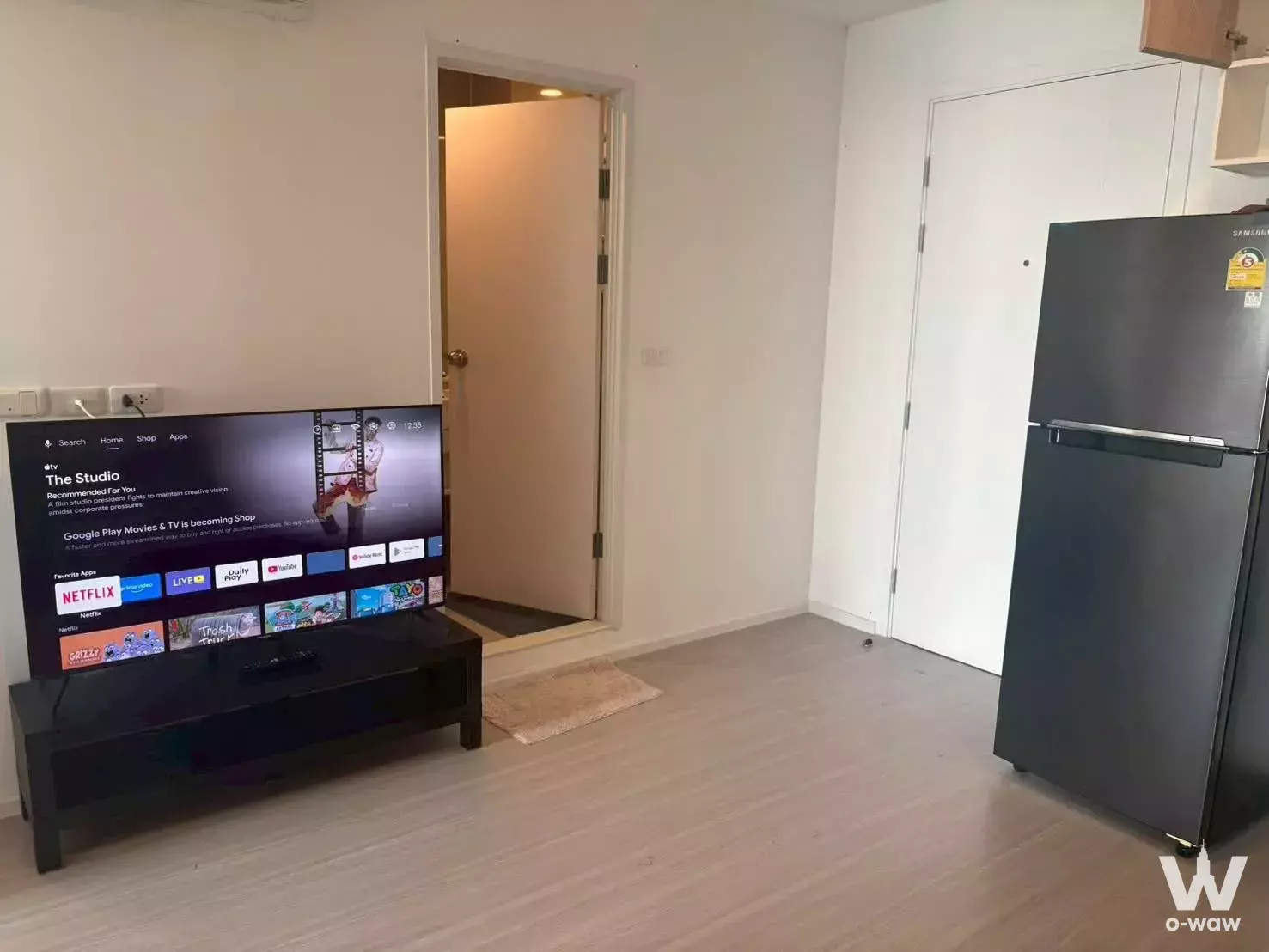 Open-plan 1-bed condo living area in DENIM Jatujak with TV stand, fridge, and light wood flooring