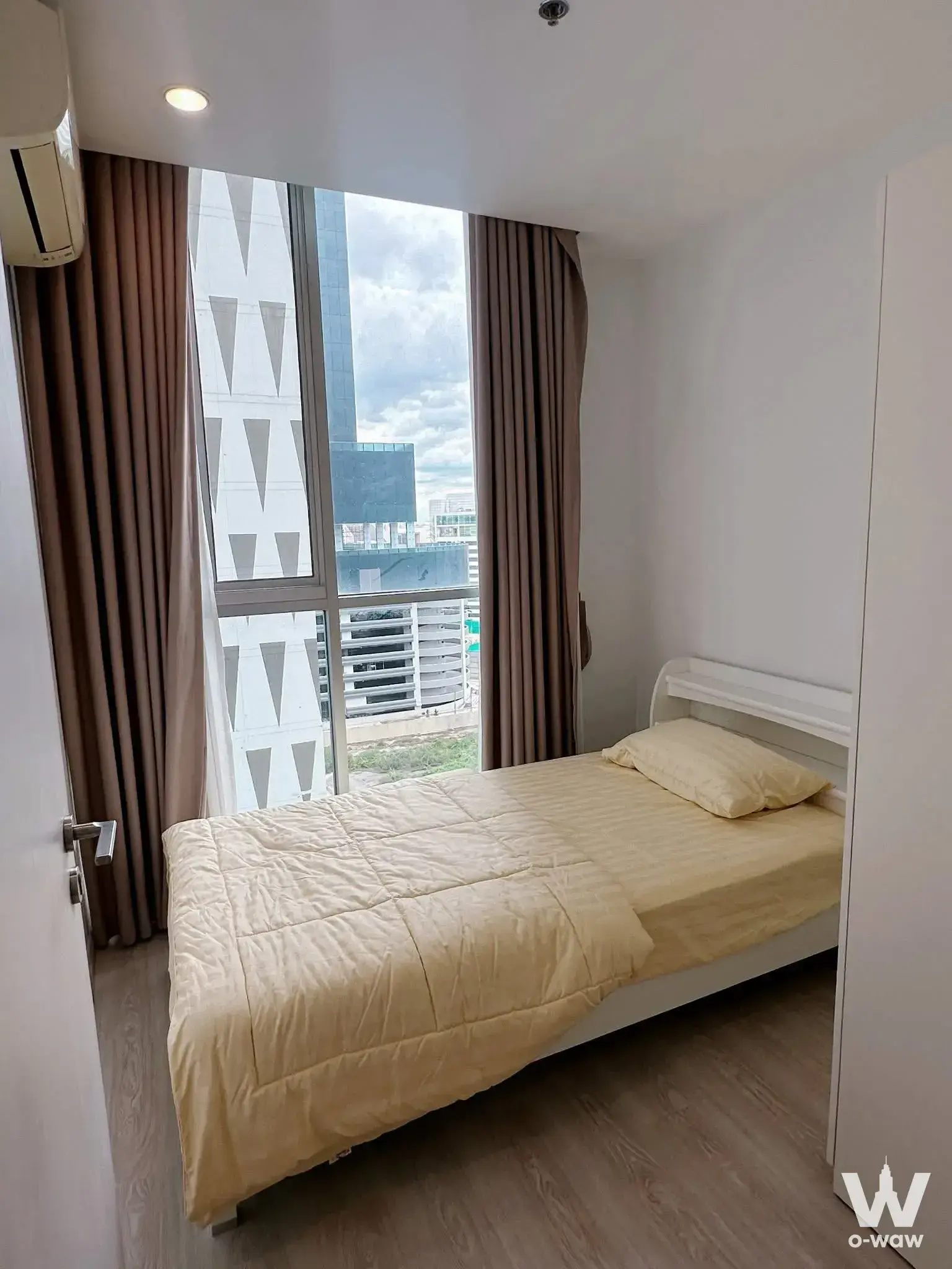 Compact bedroom in Noble Revolve Ratchada 2 with a white metal bed, yellow comforter, and floor-to-ceiling window
