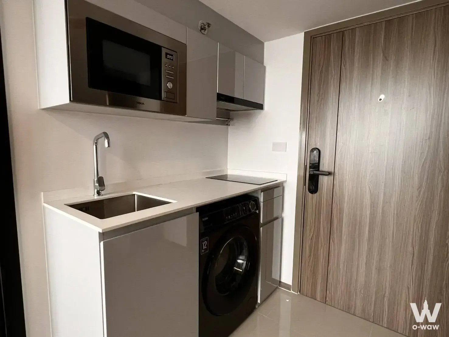 Compact kitchenette in a KnightsBridge Space condo with white cabinets, black induction cooktop, and washer