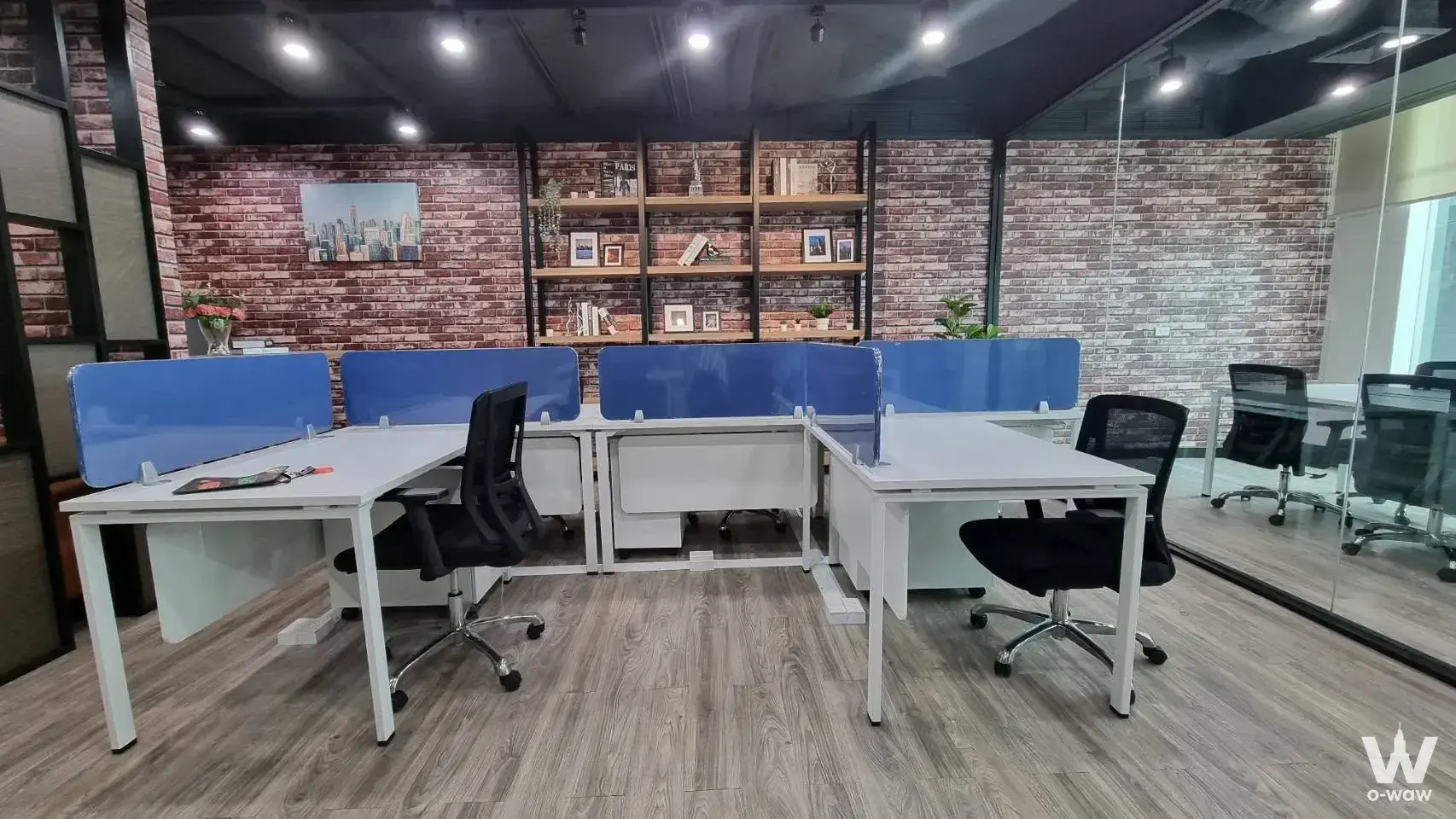 Industrial office space at INTERCHANGE 21 with brick walls, four workstations, and tall wooden shelving
