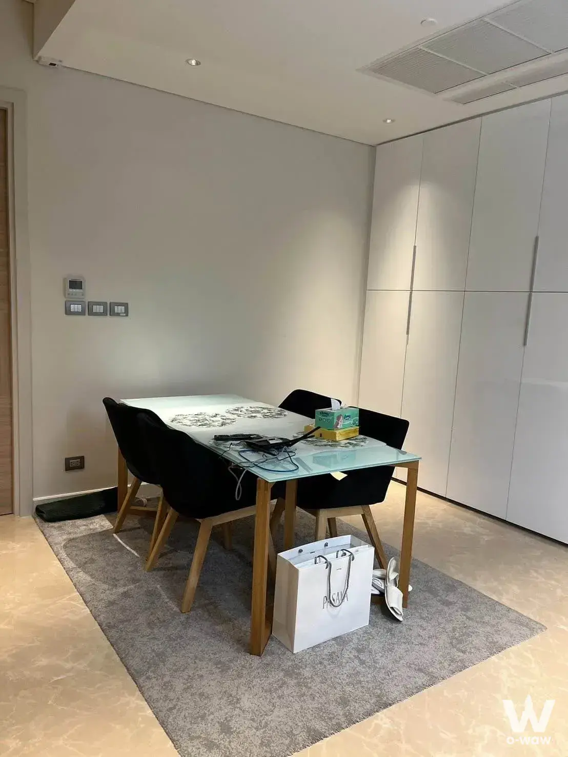Glass-top dining table with black chairs beside a white wardrobe wall in Sindhorn Residence 2-bed condo