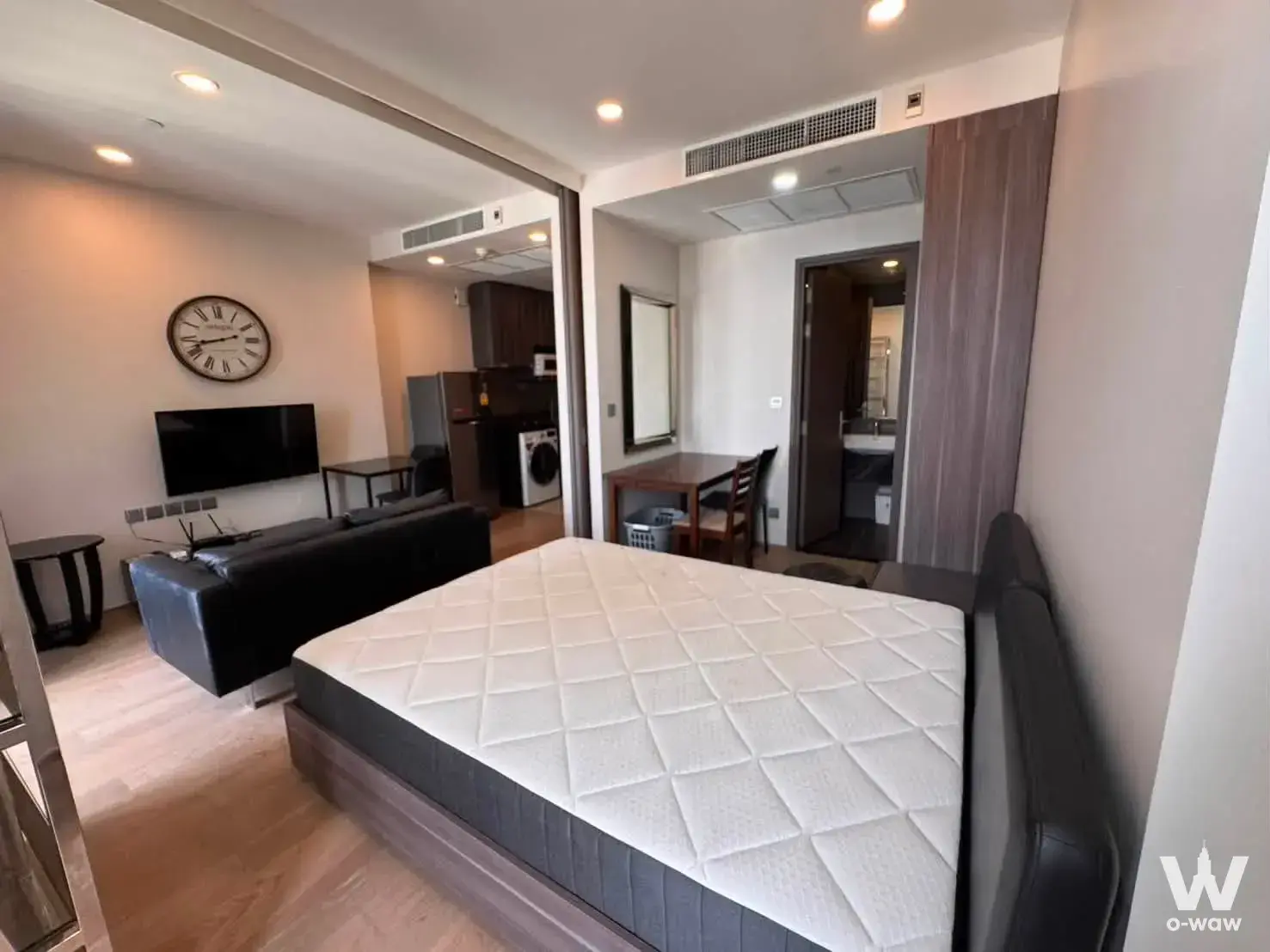 Open-plan studio in Ashton Chula-Silom with queen bed, black leather sofa, and dark wood kitchen