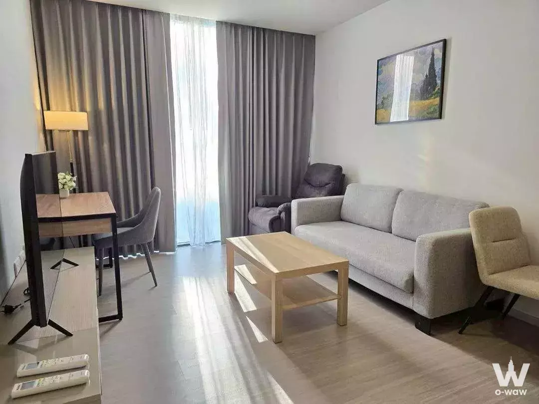 Living room in Quintara Treehaus Sukhumvit 42 condo with grey sofa, wood desk, and natural daylight