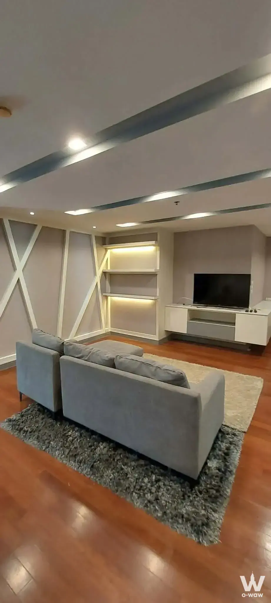 Modern 3-bed condo living room in Belle Grand Rama 9 with grey sofas, wood-look floors, and warm LED lighting