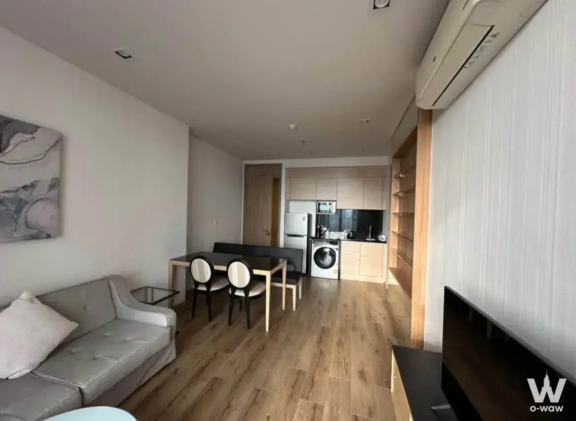 Grey leather sofa and dining nook in this Park Origin Phrom Phong 2-bed rental with built-in wood shelving