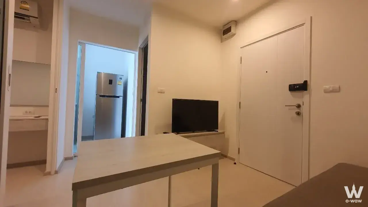 Open-plan living area in Aspire Erawan Prime condo featuring light wood floors and a smart-lock entry door