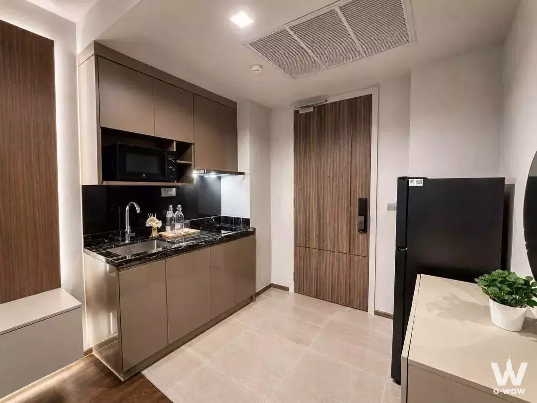 Compact kitchenette featuring taupe cabinets, black granite counters, and a smart lock in Ideo Q Sukhumvit 36