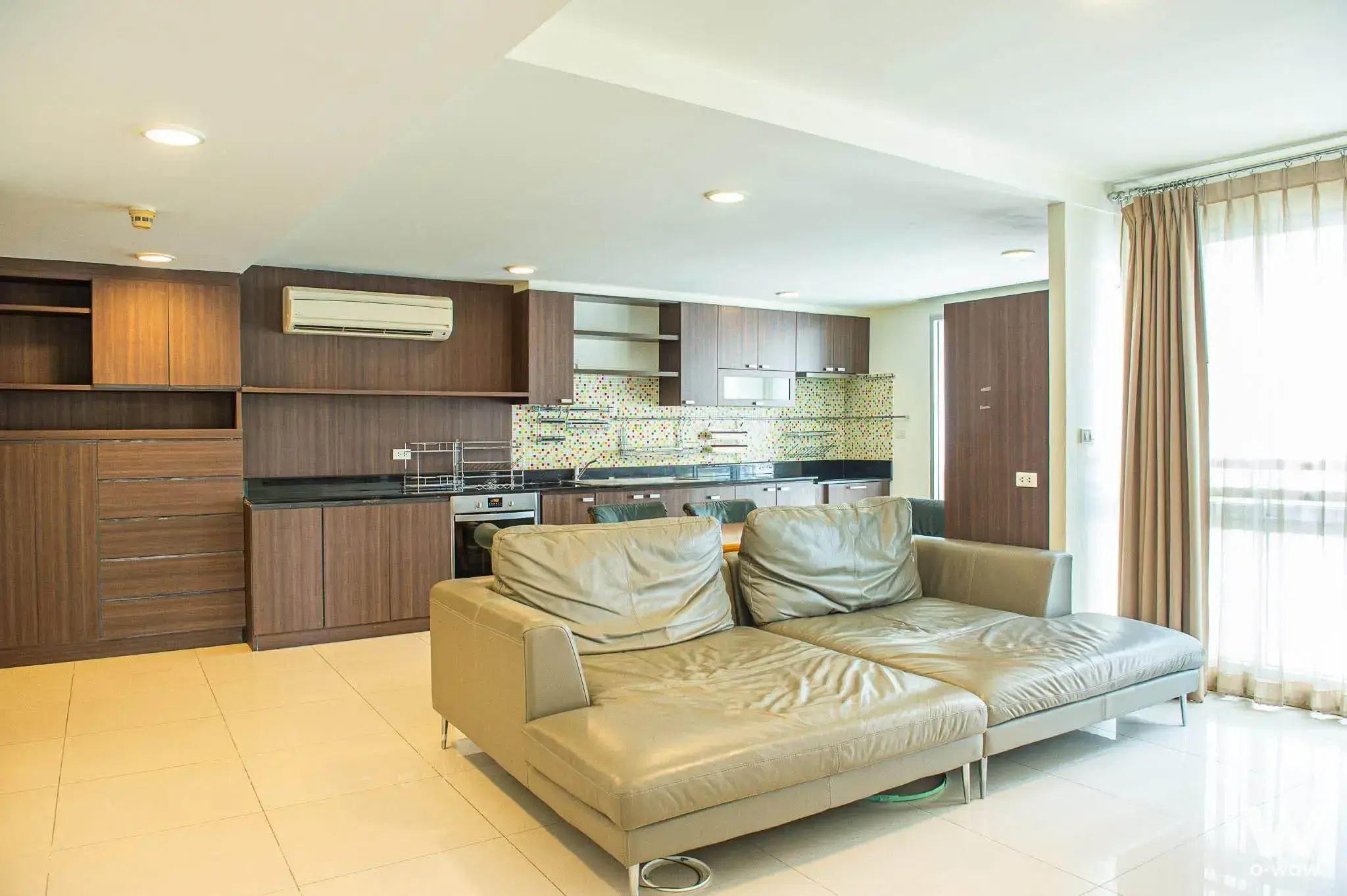 Open-plan living kitchen in a 3-bed Harmony Living house for rent with beige leather sofa and mosaic backsplash