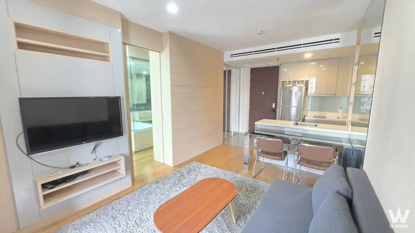 The Address Asoke one-bedroom condo open-plan living room with grey sofa, TV unit, and kitchen island
