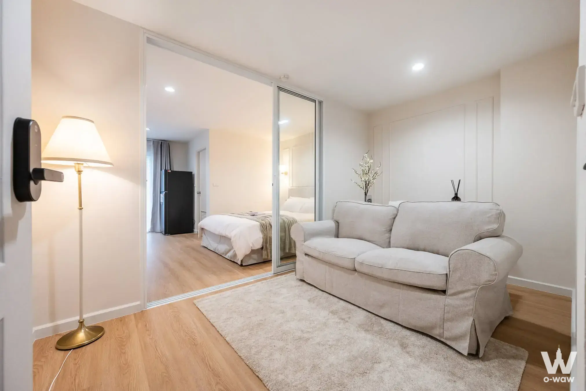 Studio living area in Grand Park Town 1-bed condo featuring beige sofa and sliding glass partition