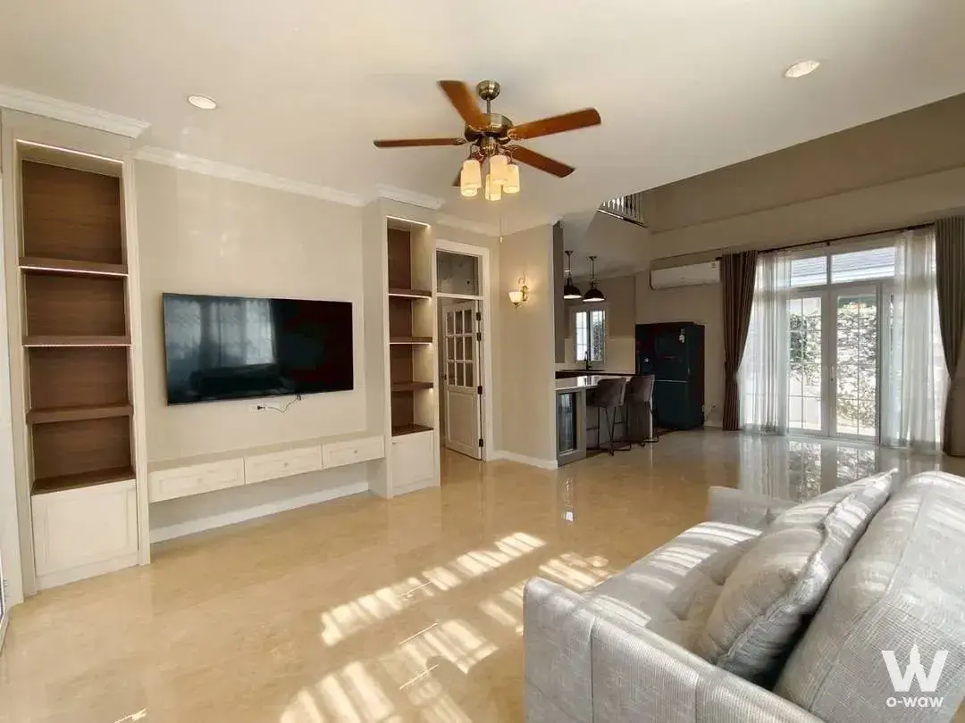 Living room in Fantasia Villa2 house with beige tile floors, grey sofa, TV unit, and view of outdoor greenery