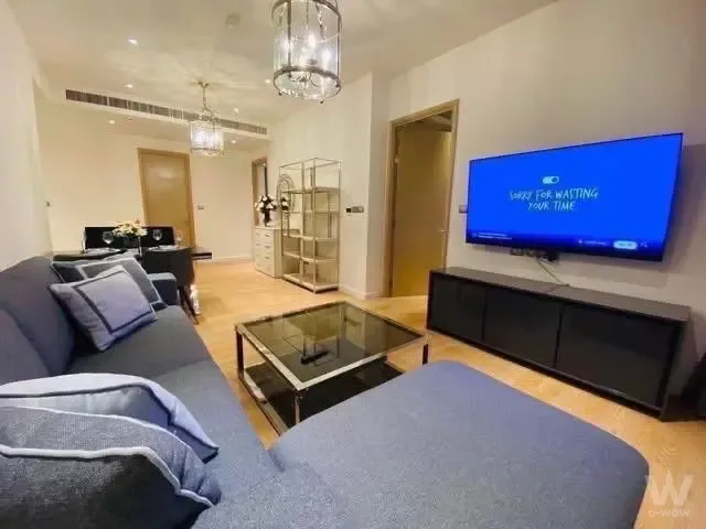 Staged 2-bed condo living room in Magnolias Waterfront Residences with crystal chandeliers and blue-grey sectional sofa