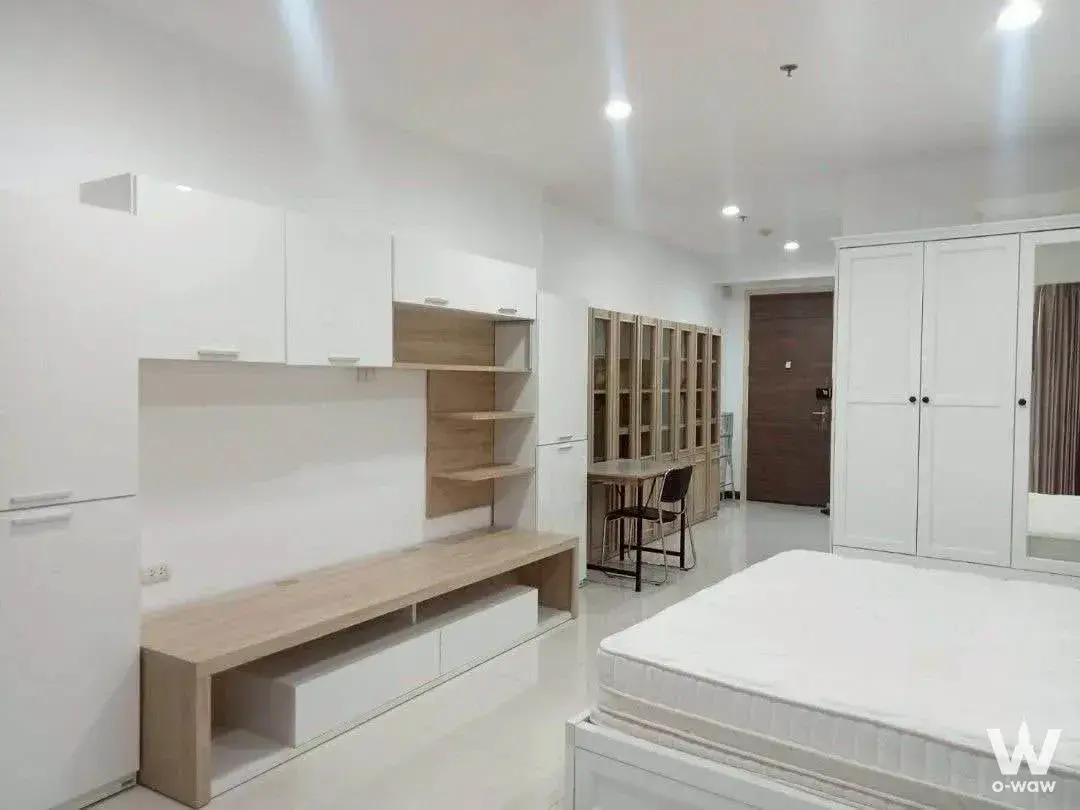 Empty bedroom in Supalai Prima Riva with white platform bed, built-in oak shelving and mirrored wardrobe on tile floor
