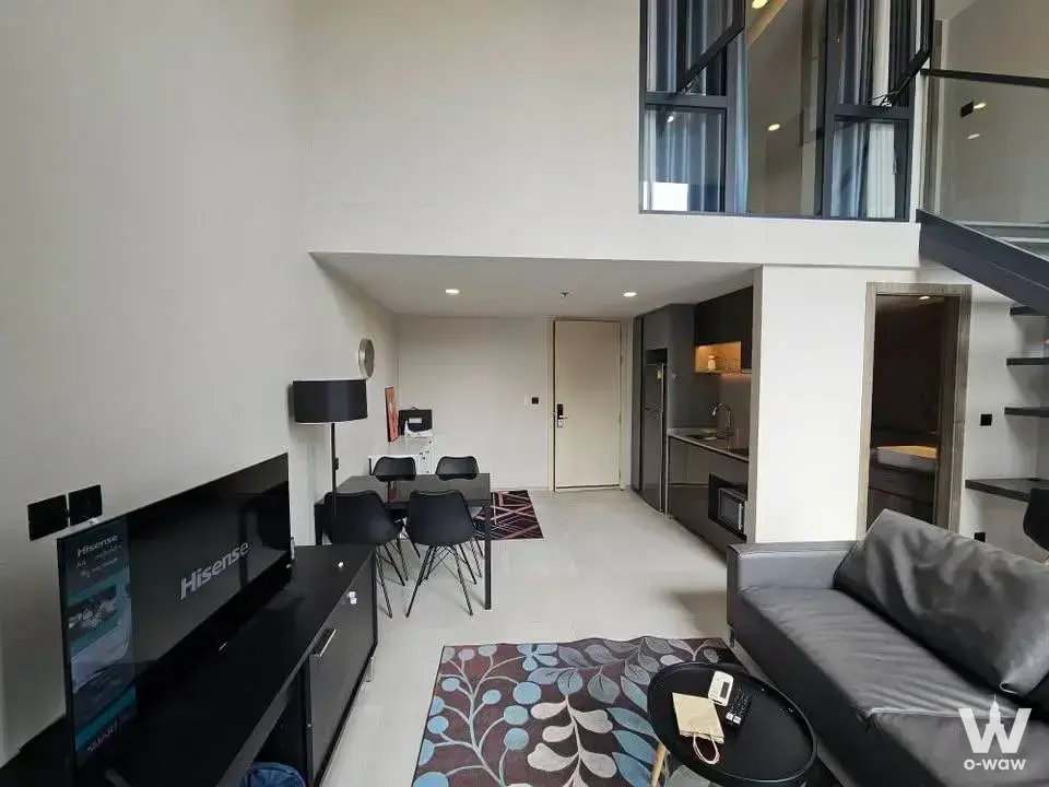Duplex loft living area in Cooper Siam with a dark grey sofa and open staircase leading to the mezzanine