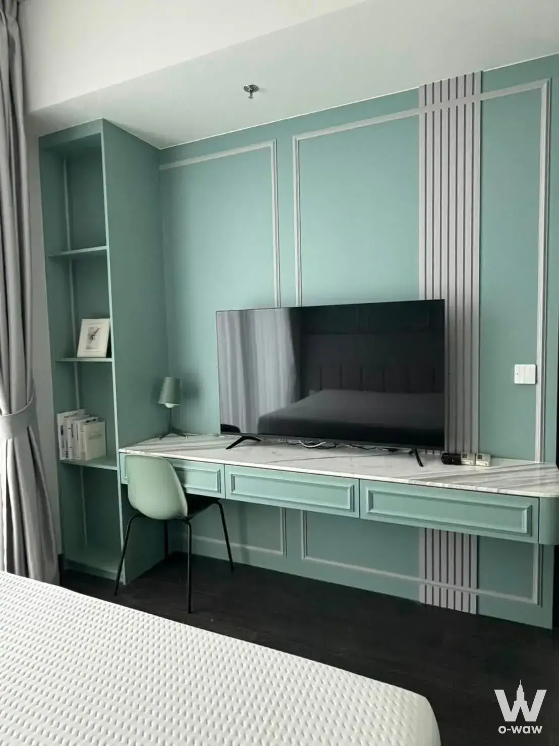 Mint-green bedroom corner in Tait Sathorn 12 with a floating desk, TV console, and floor-to-ceiling shelving