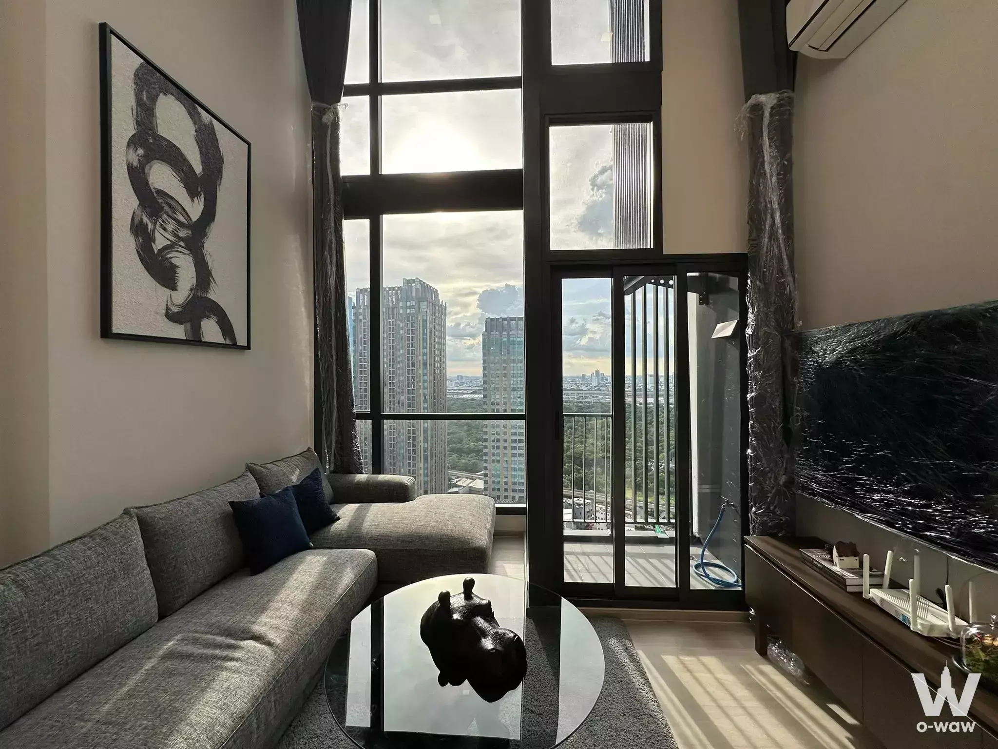 Living room in The Privacy Jatujak condo with a grey sectional sofa and floor-to-ceiling windows overlooking the city