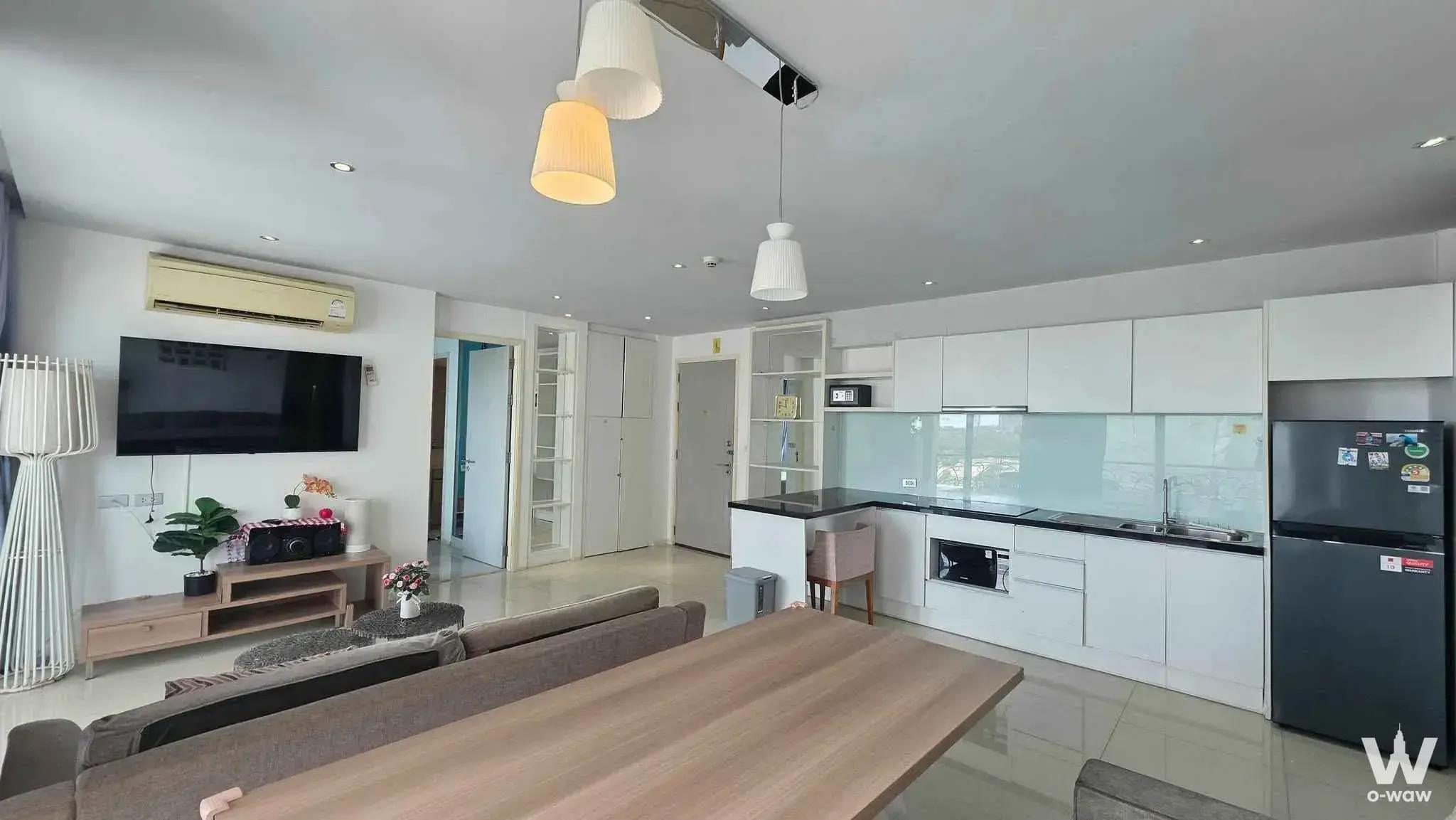 Open-plan living room with grey sectional and white kitchen in this 2-bed condo for rent at Atlantis Condo Resort Pattaya