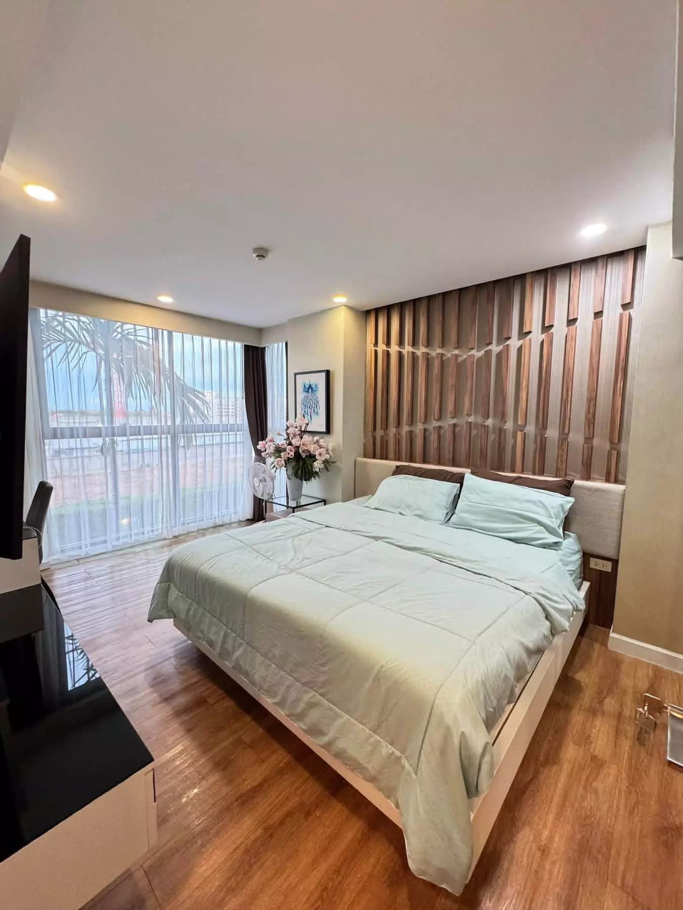 Dusit Grand Park 2-bed condo bedroom featuring mint-green bedding, wood-slat wall, and balcony view