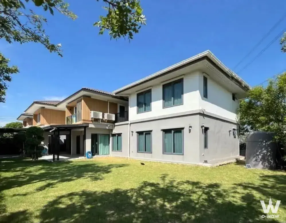 Two-story detached house exterior with white stucco walls, grey concrete finish, and manicured lawn in Viranya Wongwaen -