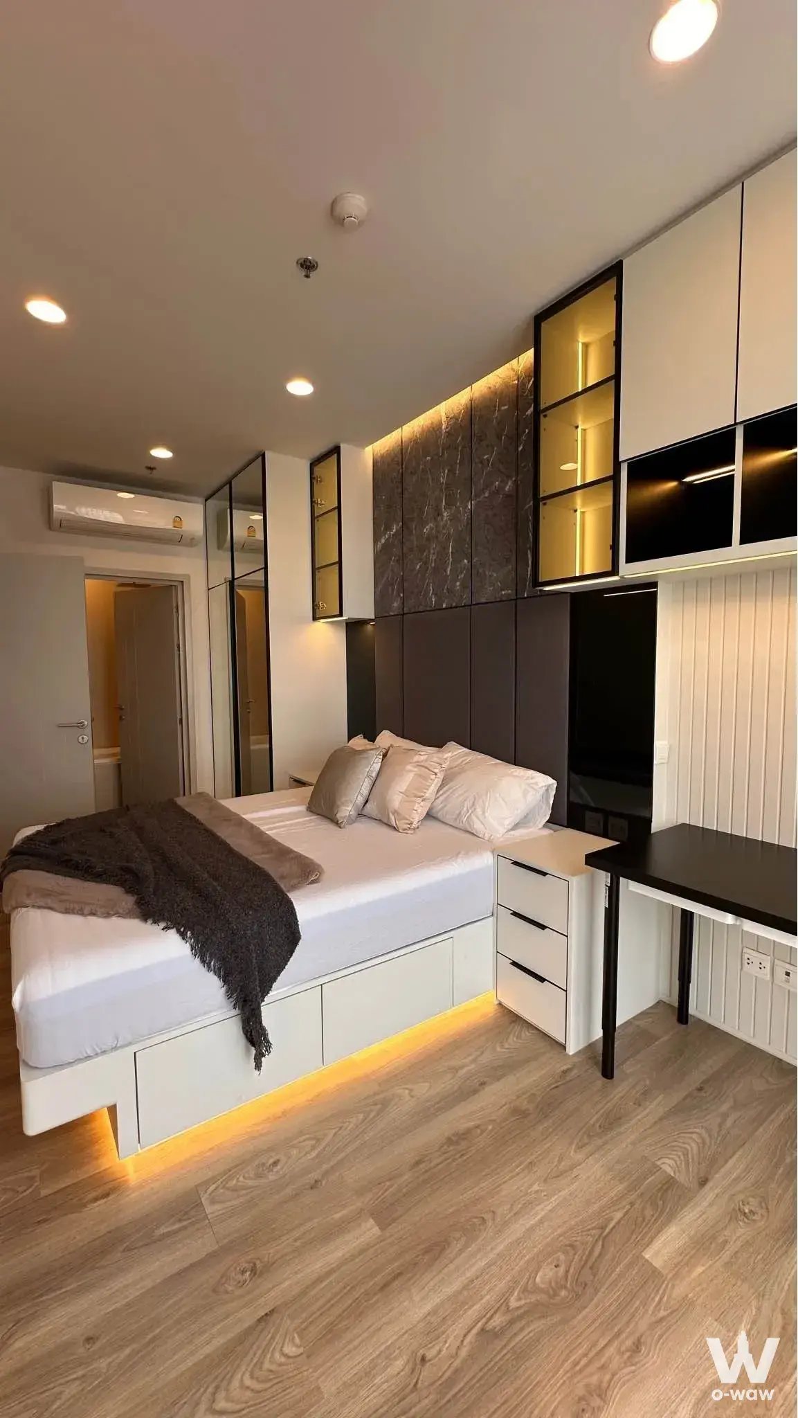 1-bed condo for rent in Oka Haus bedroom with floating bed, LED lighting, and dark grey built-in wall unit