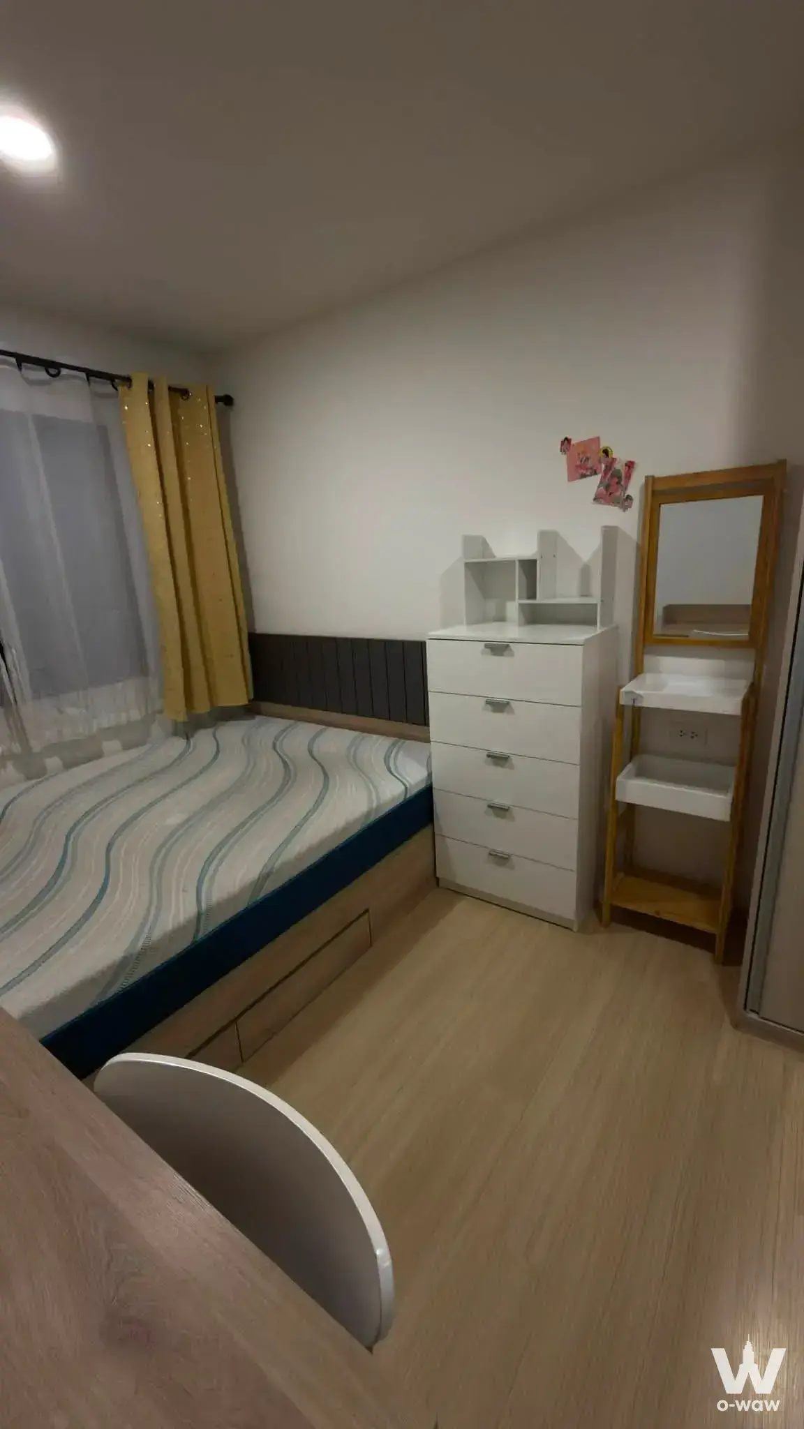 Bedroom in a Chewathai Hallmark Ladprao condo with a low platform bed, light oak floors, and minimalist white furniture