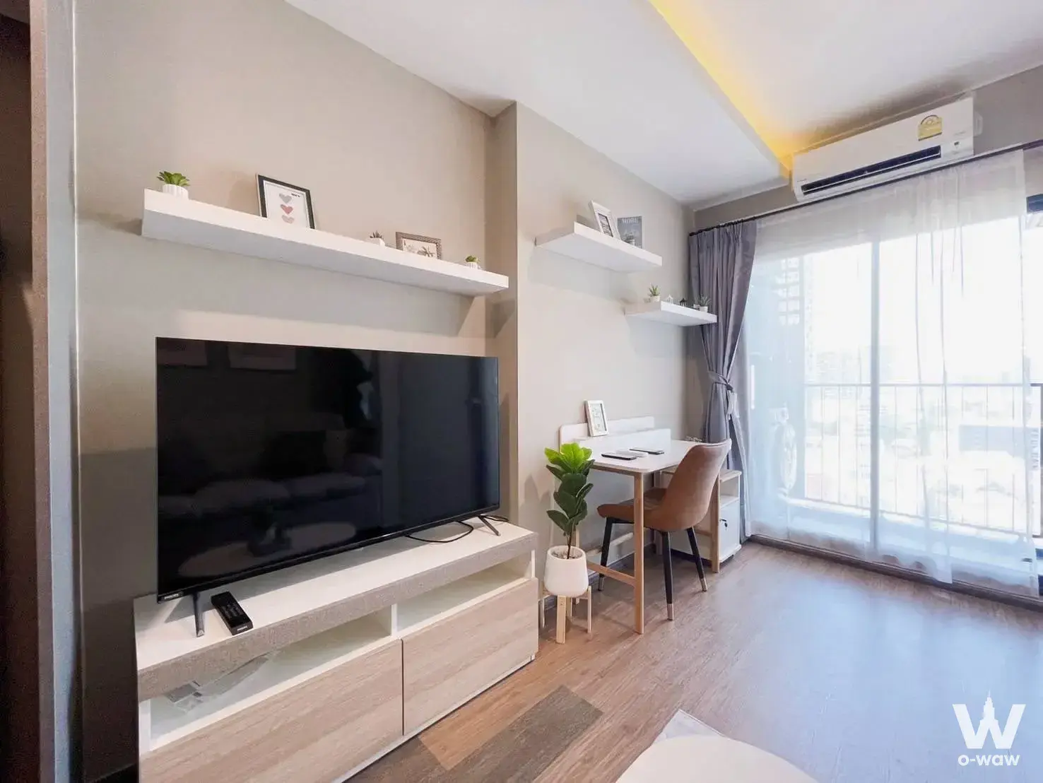 Bright living space in Ideo Sukhumvit 93 featuring light wood floors, floating shelves, and a high-rise view