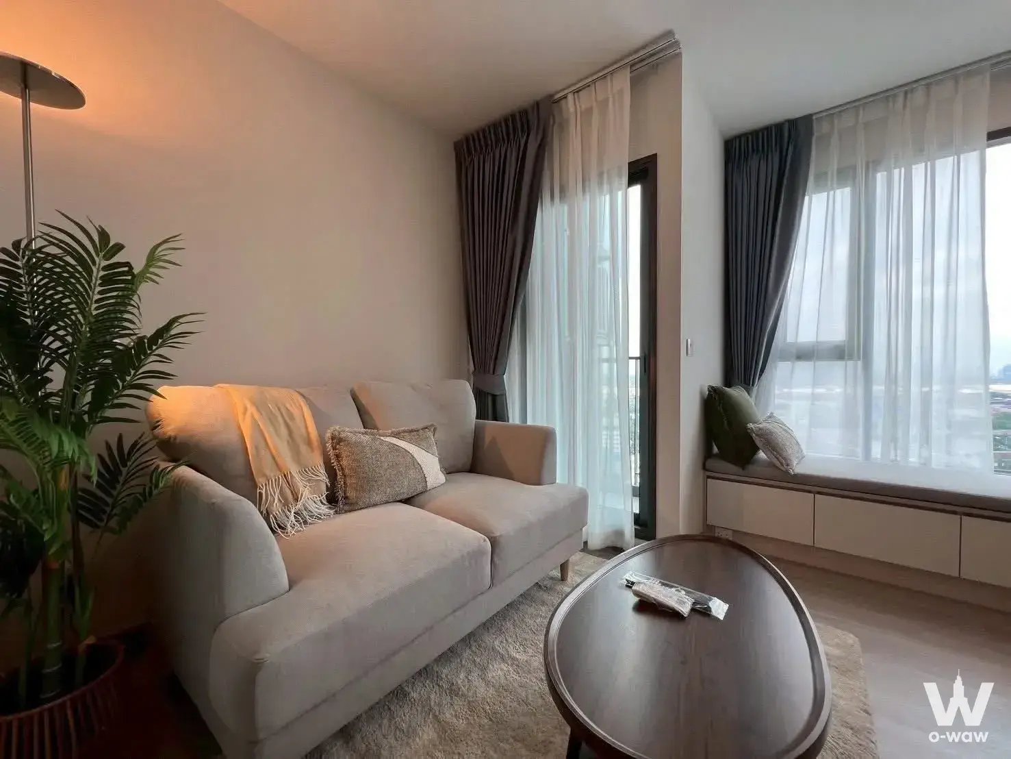 Cozy living room in Aspire Sukhumvit-Rama 4 featuring beige sofa and city view through glass doors