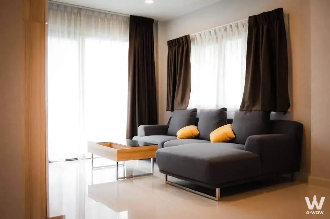 Bright living room in a modern condo for rent in Centro Bangna featuring charcoal sofa and wood table