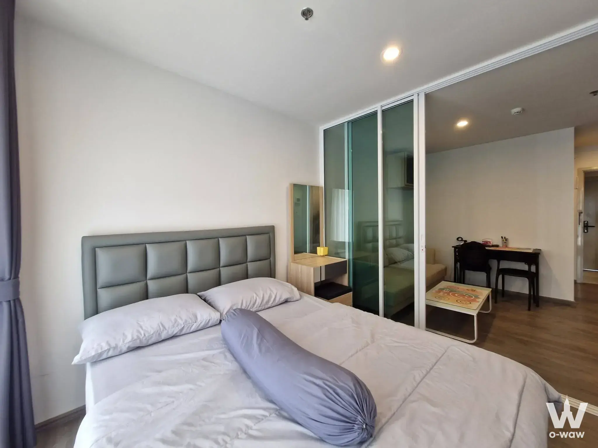 Regent Home Bangna 1-bed condo bedroom with grey upholstered bed, glass partition, and minimalist wooden furnishings