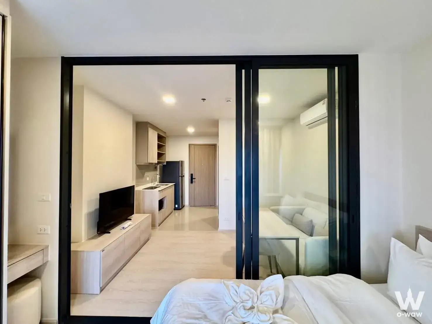 Open-plan bedroom and living area in a FLO by Sansiri 1-bed rental with glass partition and light wood accents