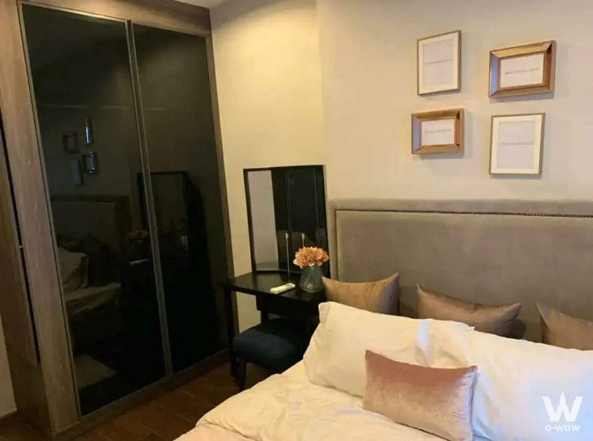 C Ekkamai bedroom with queen bed, pink velvet accent pillow, dark smoked glass wardrobe, and framed art prints on warm beige