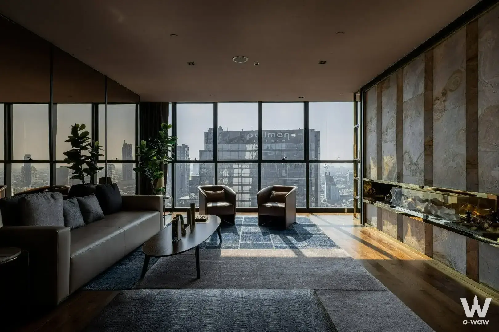 Luxury Ashton Silom living room with dark leather seating and floor-to-ceiling windows overlooking the city skyline