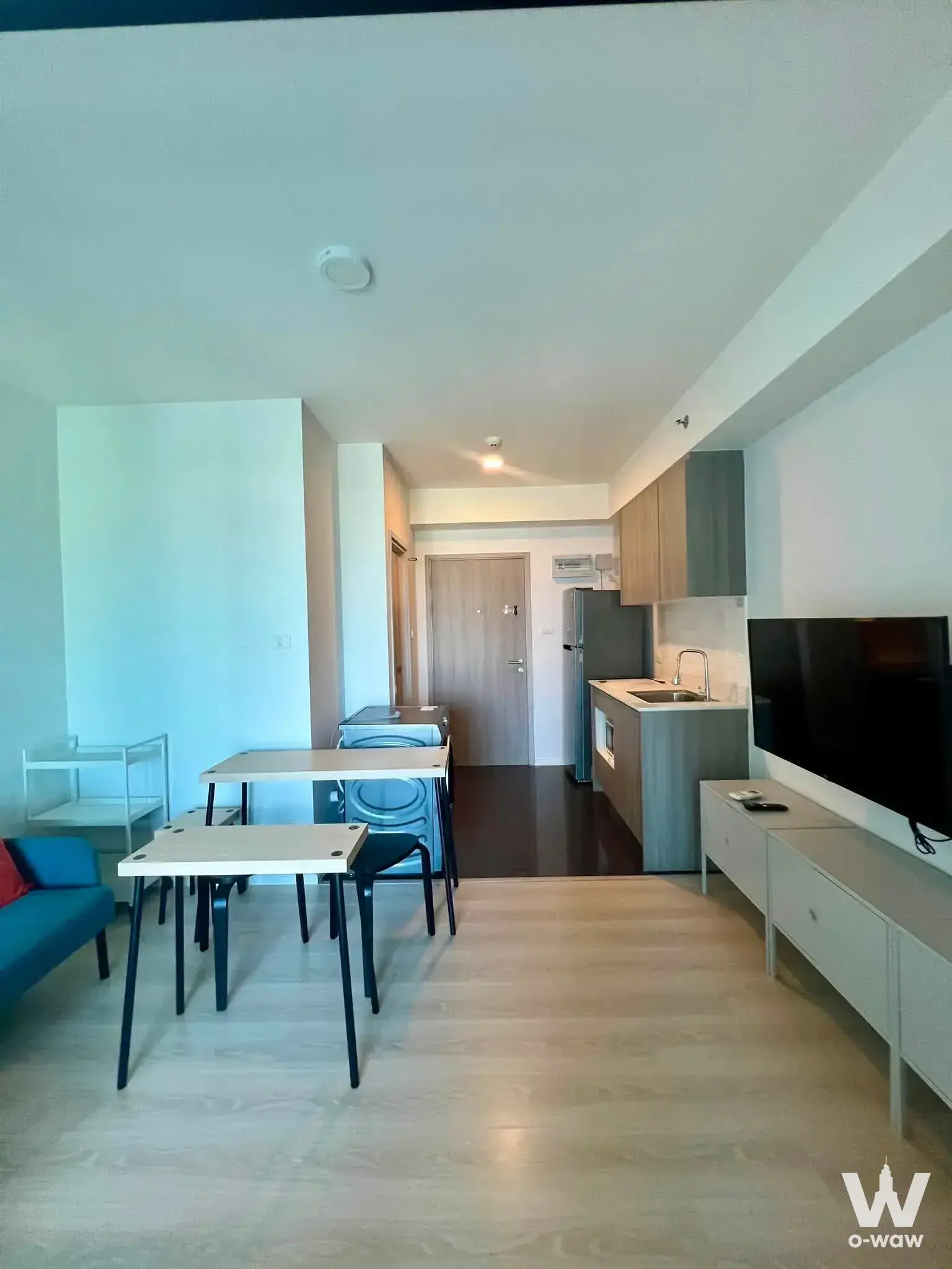 Open-plan studio at A Space Condominium featuring a teal sofa, white media console, and compact kitchen with grey cabinets