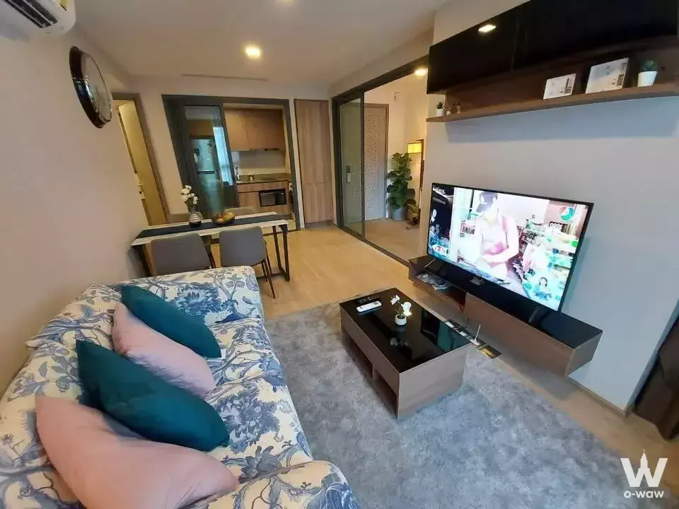 2-bed condo living room for sale in TAKA HAUS featuring floral sofa, TV, and open kitchen access