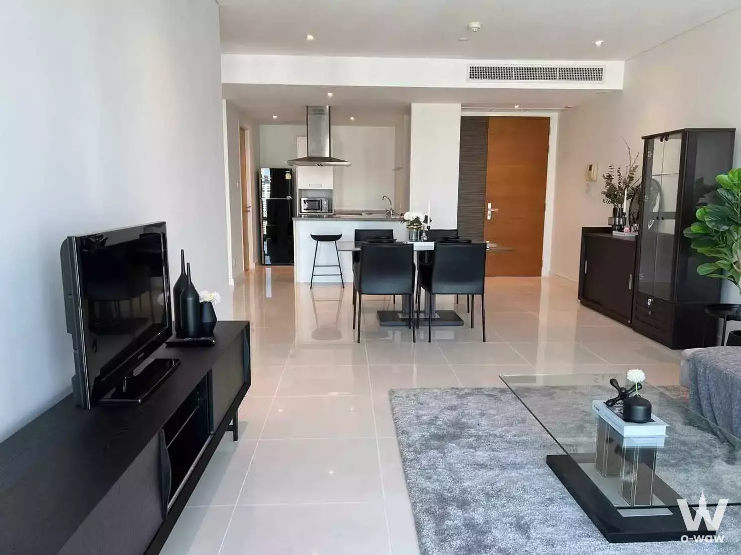 Open-plan living area featuring a glass dining table and dark wood media console in a Fullerton Sukhumvit 2-bed condo