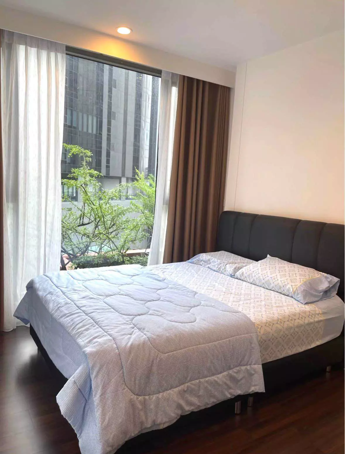 Bedroom in a Whizdom Inspire Sukhumvit condo showing a leather headboard and large window with city view