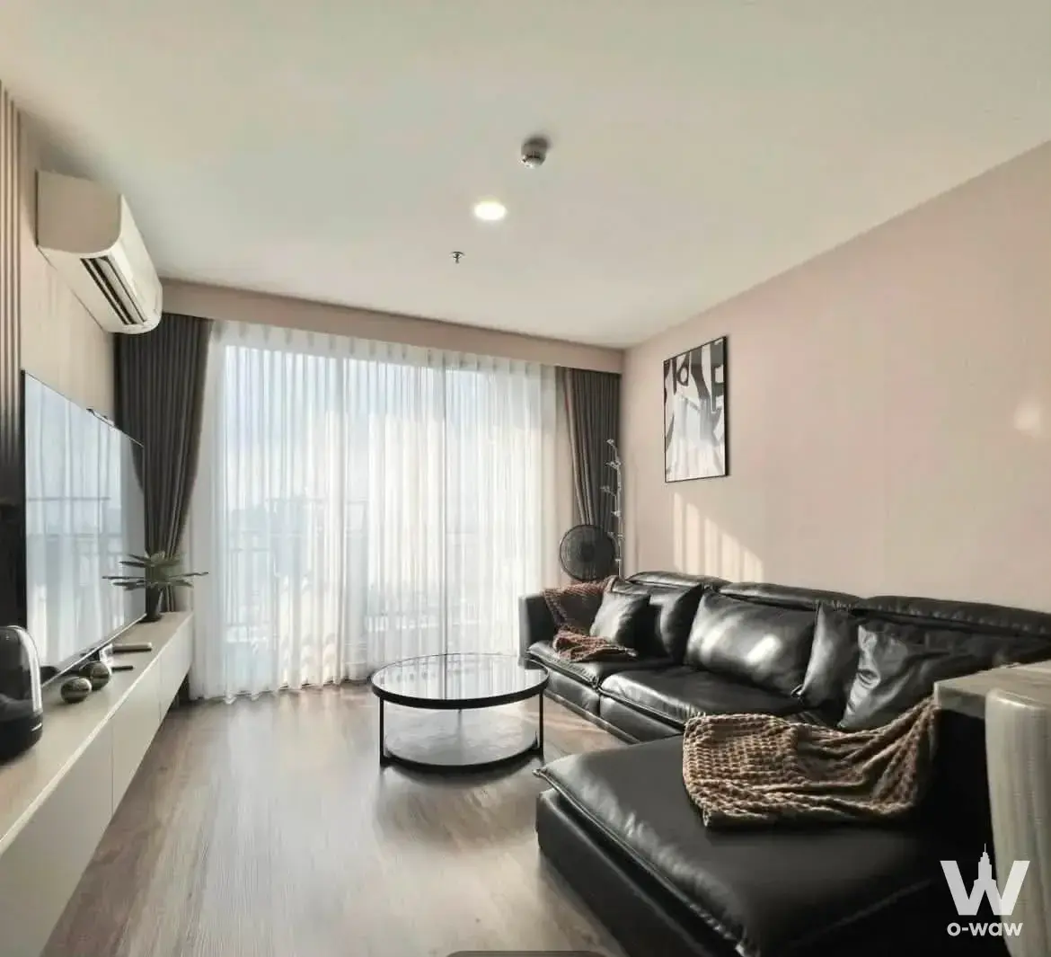 Living room in Artisan Ratchada with black leather sectional and floor-to-ceiling windows