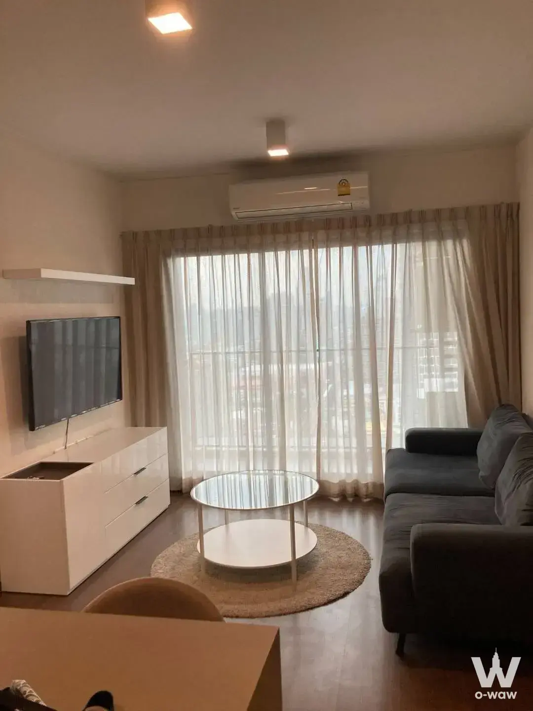Living room in a 2-bed Ideo Sukhumvit 93 condo with grey sofa and city view through sheer curtains
