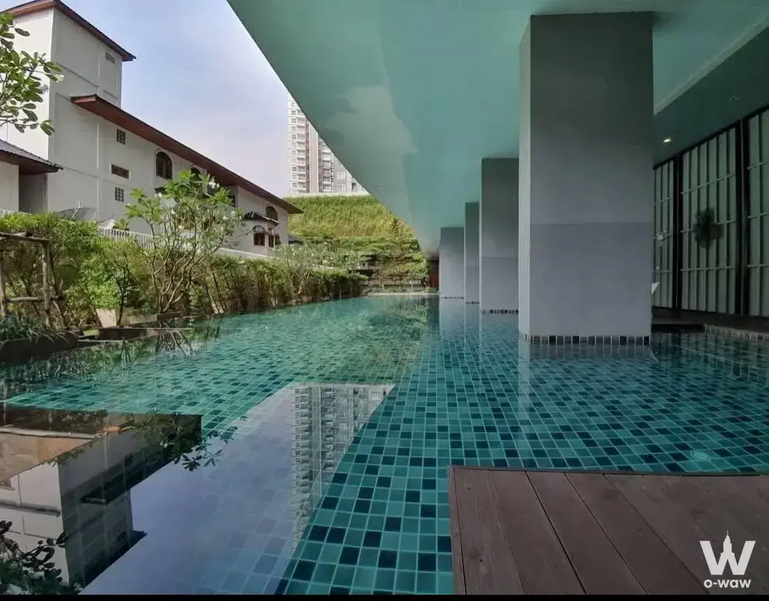 Resort-style infinity pool with teal mosaic tiles and wooden decking at Aspire Sathorn Tha Phra
