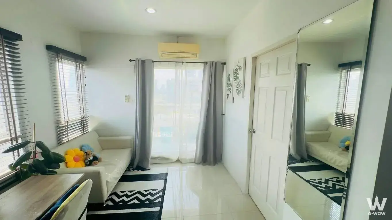 Simply furnished living room in BTS Residence Condo with cream sofa, chevron rug, and floor-to-ceiling mirror